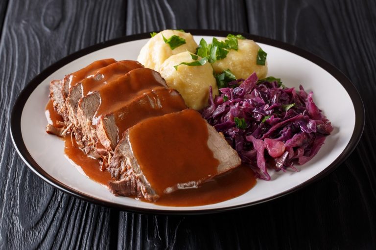 German food Sauerbraten - slowly stewed marinated beef with gravy with potato dumplings and red cabbage close-up