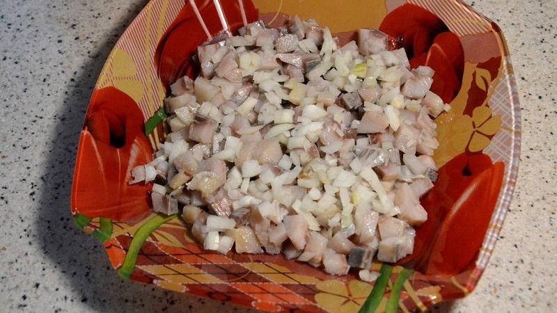 Сельдь очистить от костей и кожицы, нарезать небольшими кусочками и выложить первым слоем. Лук мелко нарезать и выложить на слой сельди